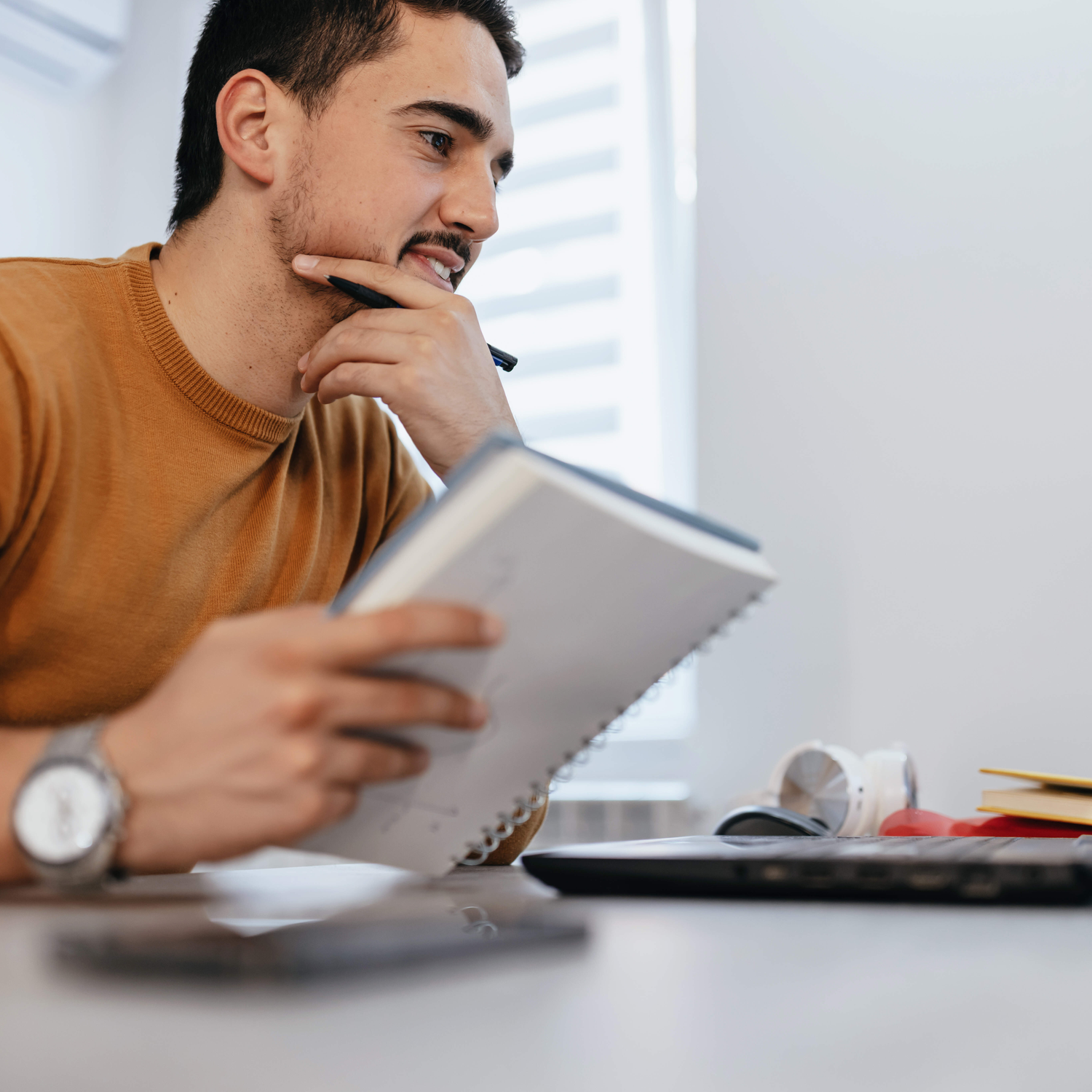 Mann sitzt vor einem Laptop und macht sich Notizen in einem Notizheft.