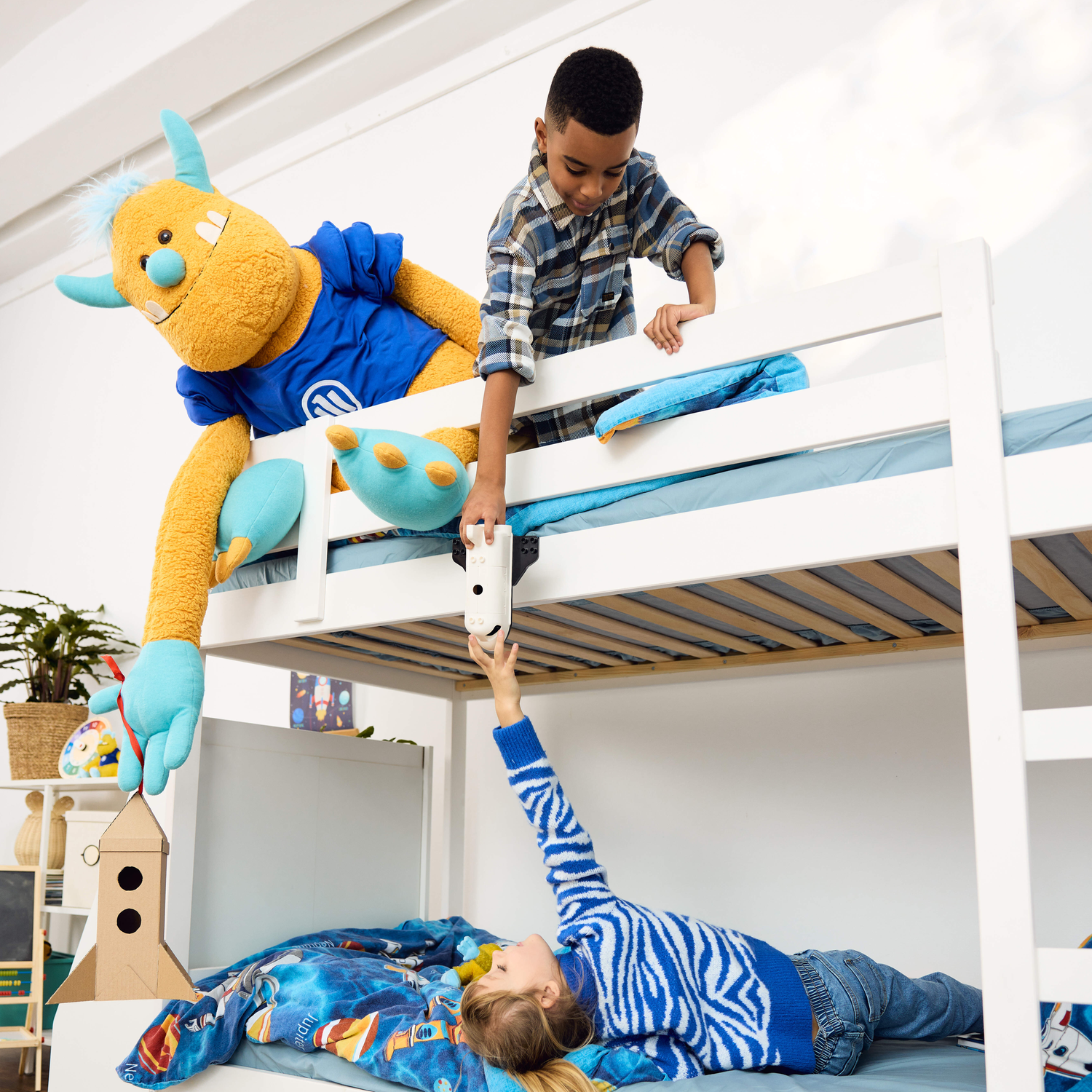 Kinder in einem Hochbett reichen sich einen Gegenstand. Das Allianz Plüschtier schaut zu.