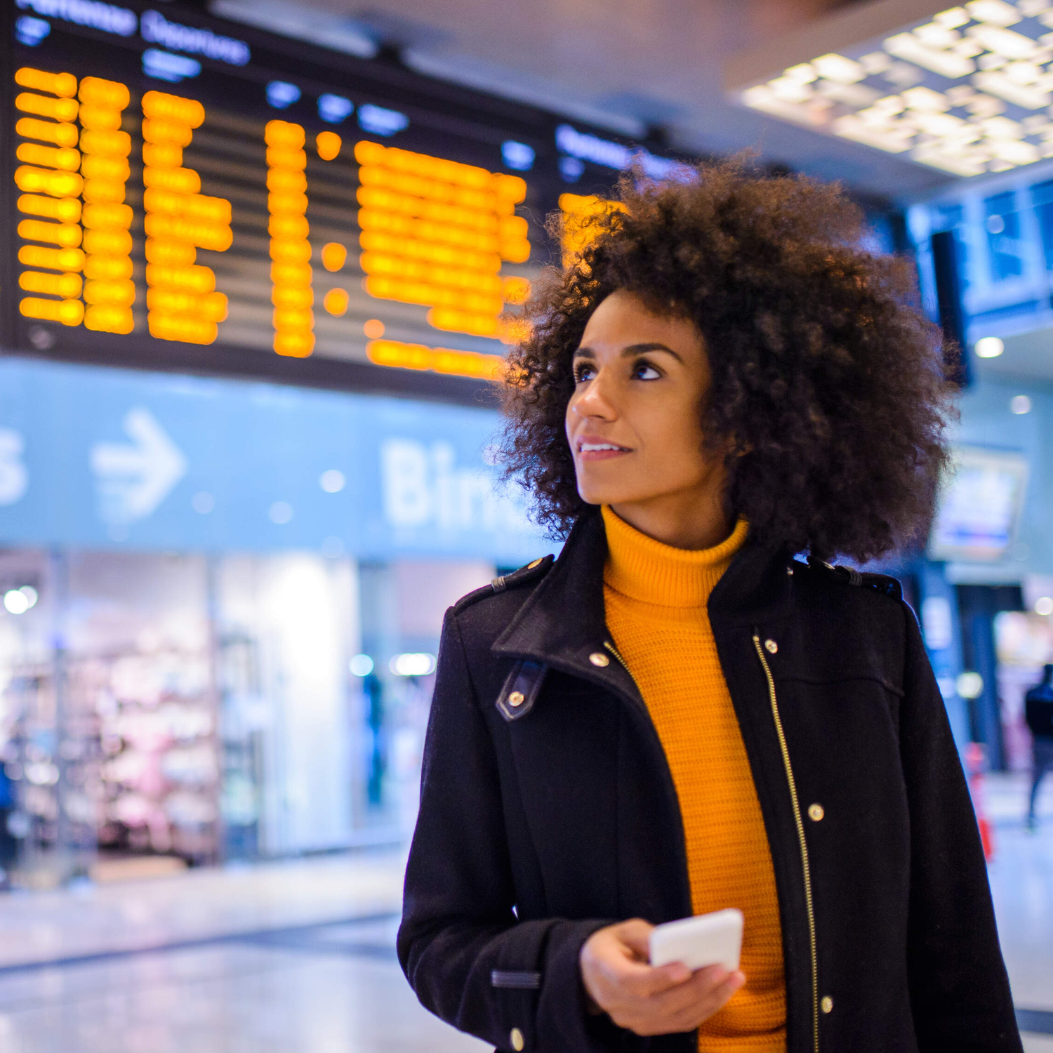 Afroamerikanische Frau auf dem Bahnhof, die die Abfahrtstafel kontrolliert
