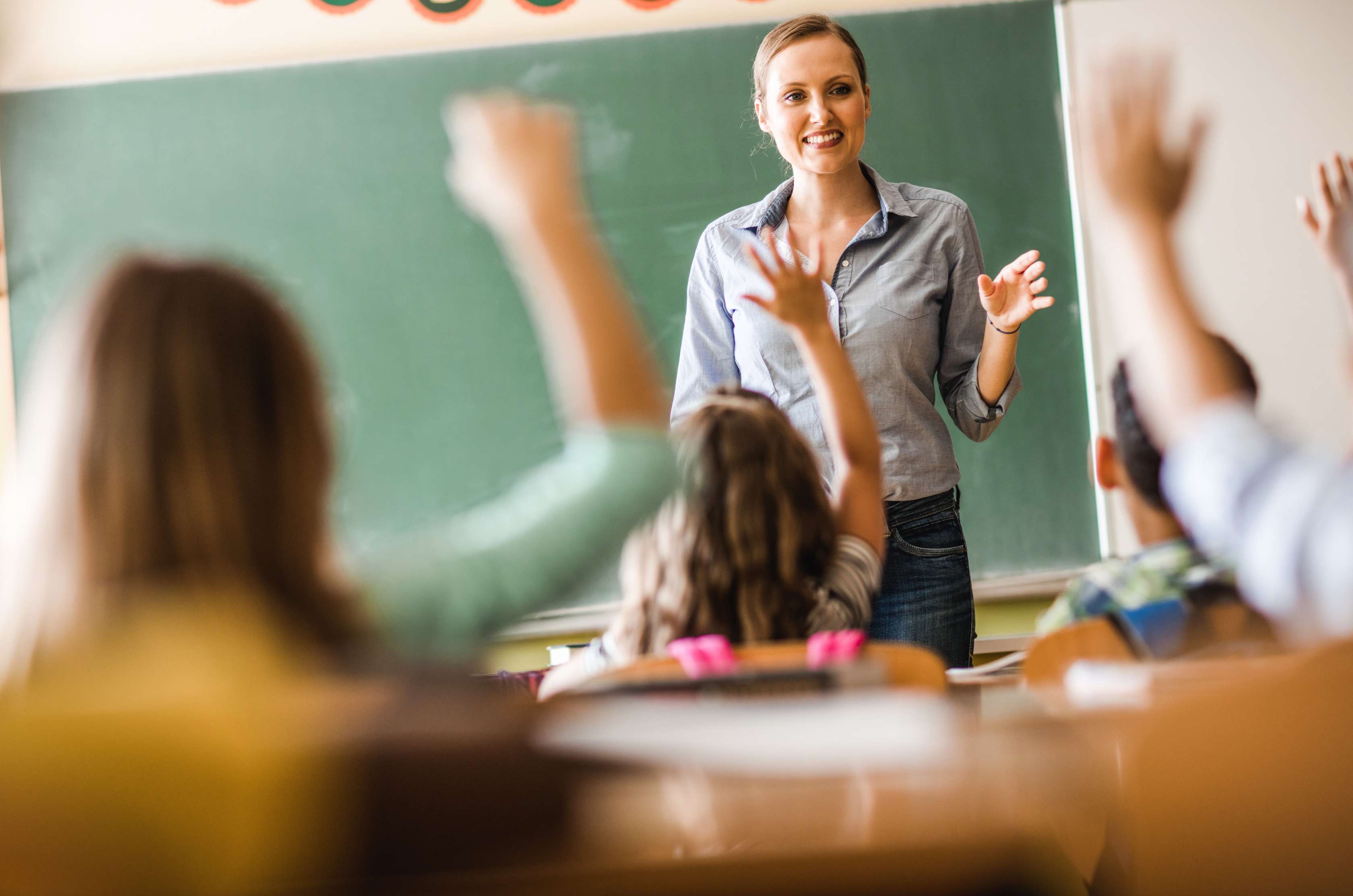 Das Bild ist urheberrechtlich geschützt. Eine Nutzung ohne vorherige Einwilligung ist nicht gestattet. eine Lehrerin steht vor der Klasse und Kinder melden sich
