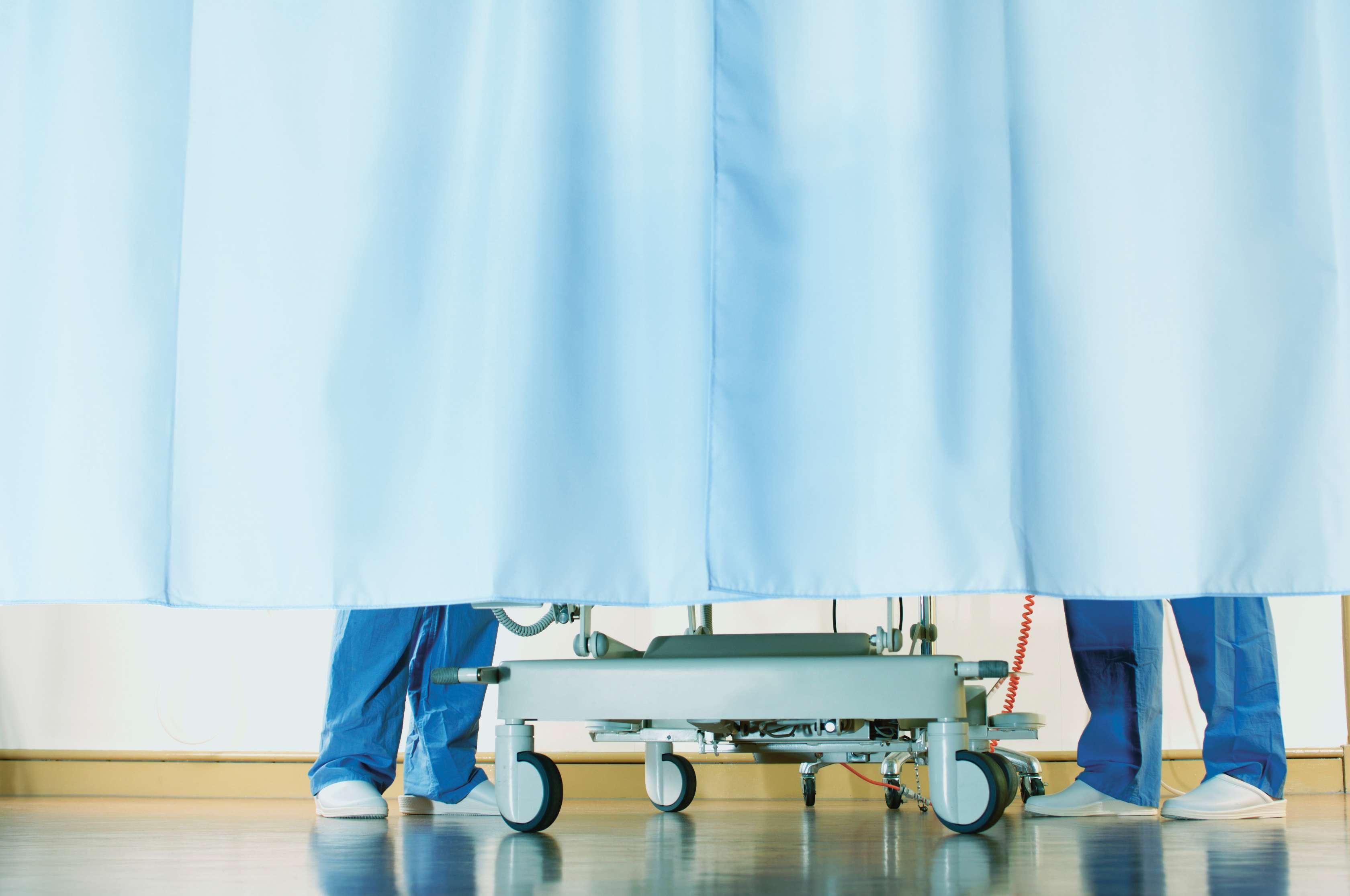Zwei Personen stehen neben einem Krankenbett hinter einem Vorhang