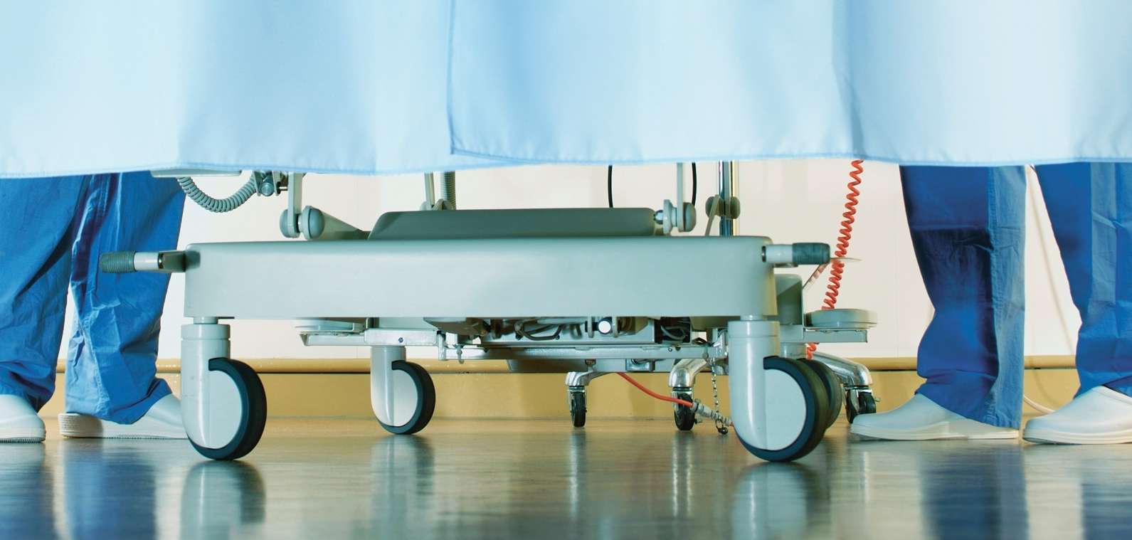 Zwei Krankenhausmitarbeitende stehen neben einem Krankenbett hinter einem Vorhang