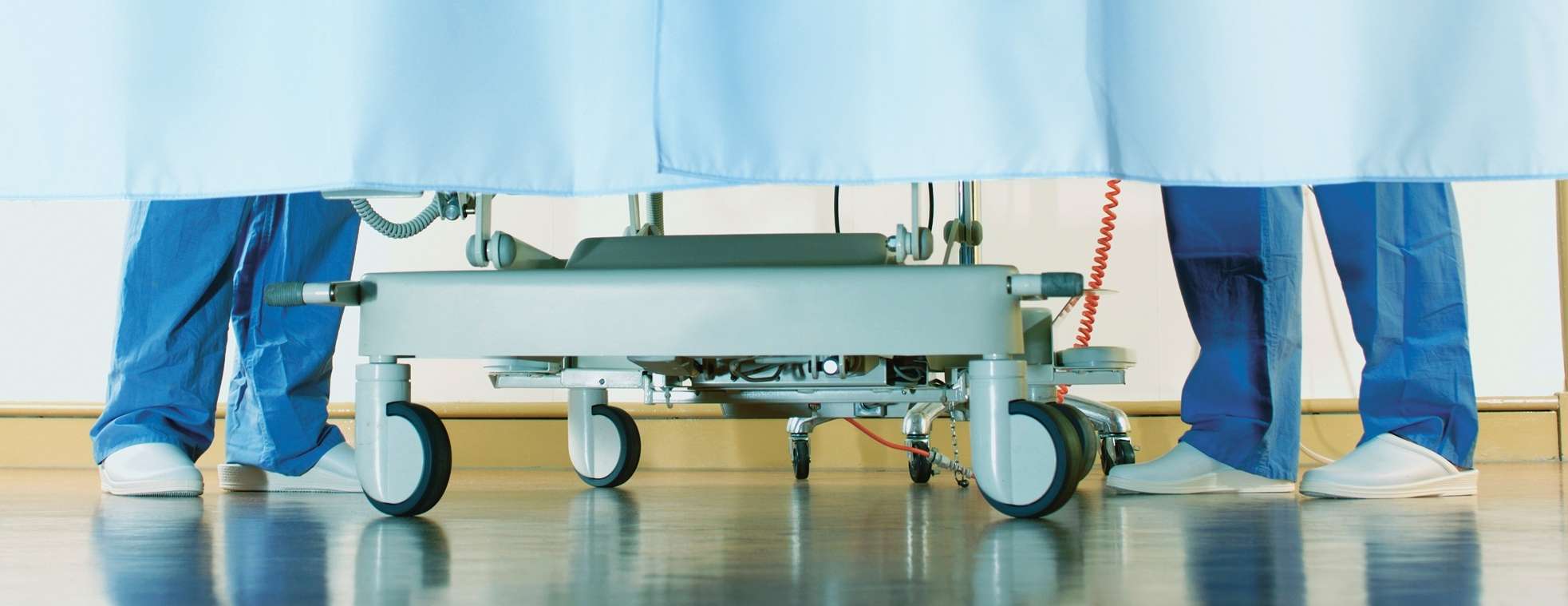 Zwei Krankenhausmitarbeitende stehen neben einem Krankenbett hinter einem Vorhang.