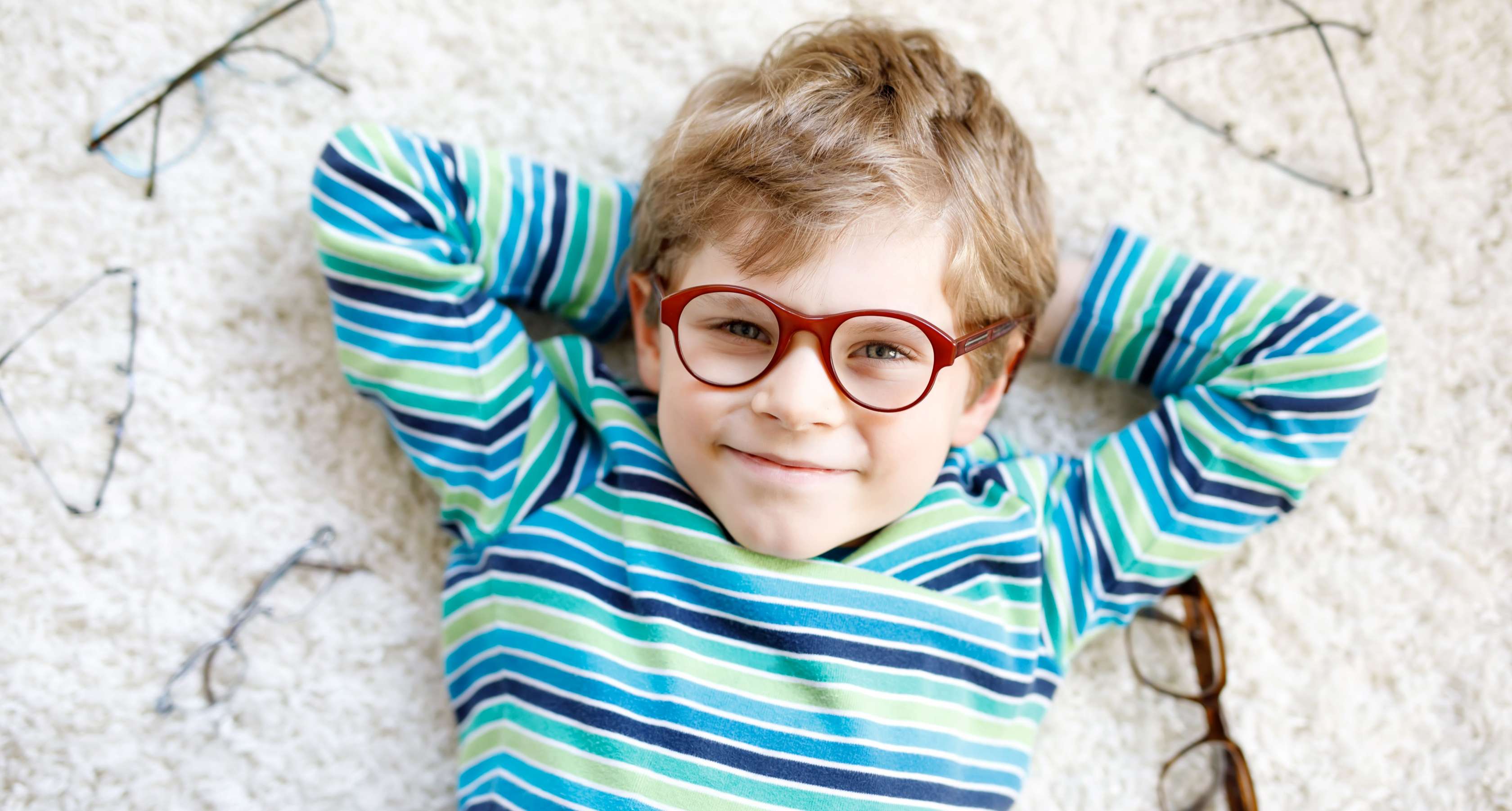 Junge mit Brille liegt lächelnd auf einem Teppich
