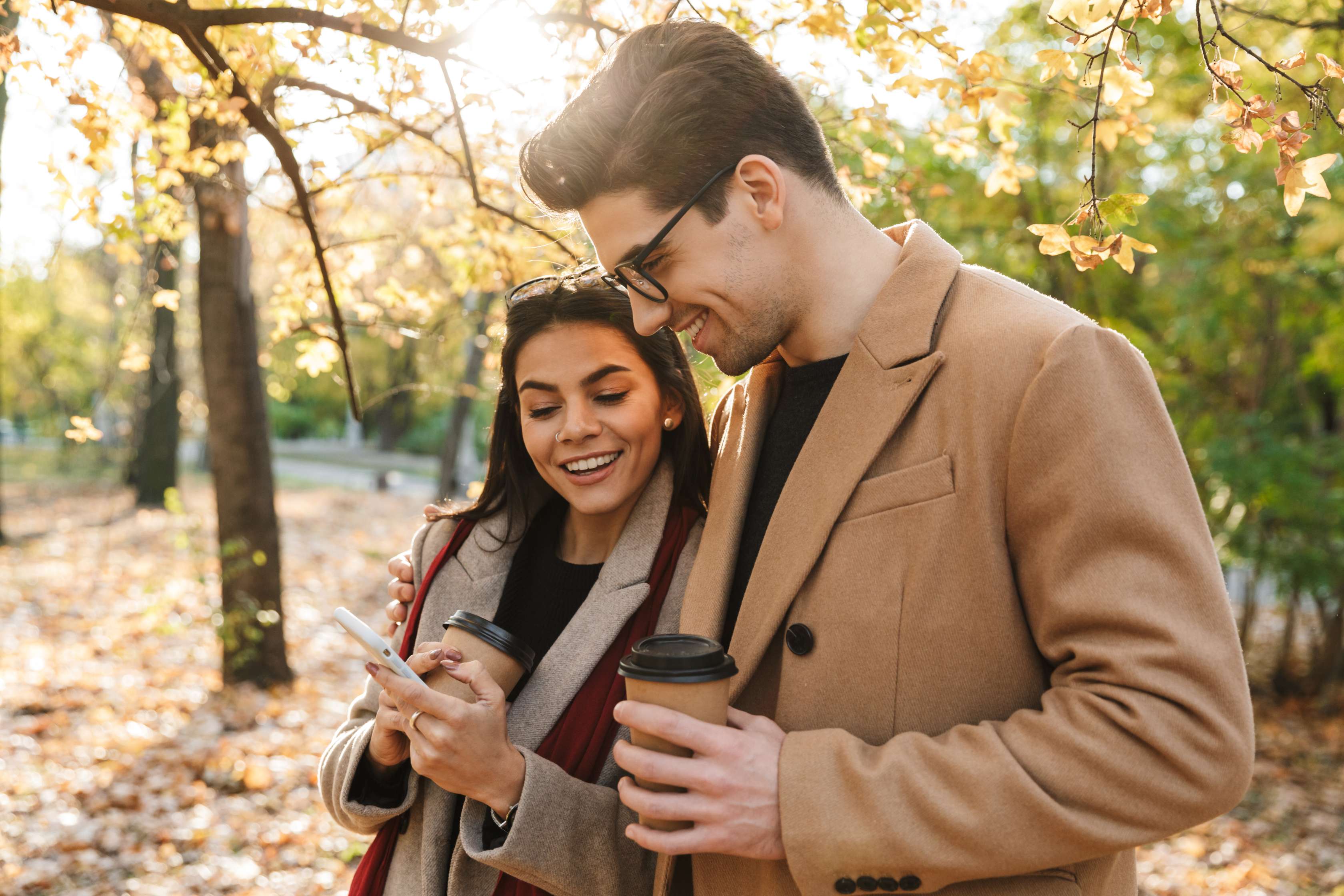 Junges Paar im sonnigen, herbstlichen Wald guckt sich zusammen auf dem Handy etwas an