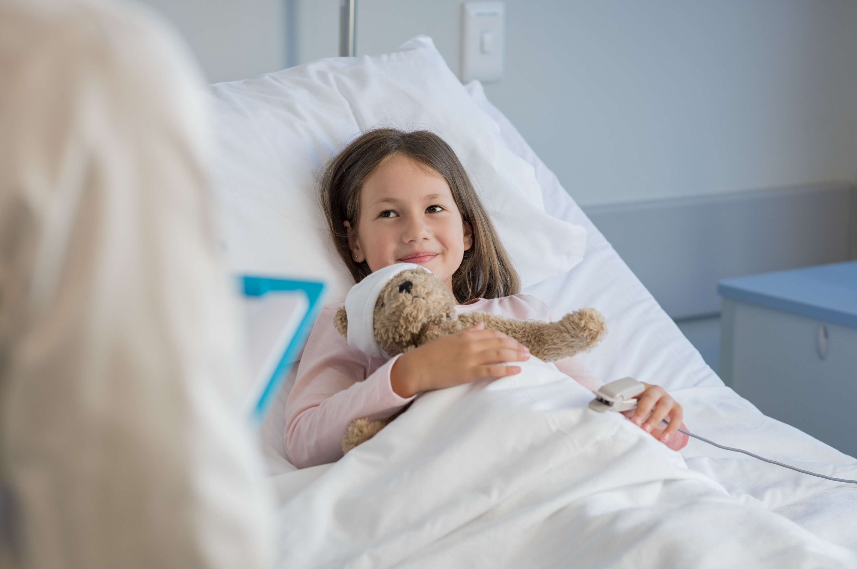 Kleines Mädchen liegt mit ihrem Teddy im Krankenhausbett