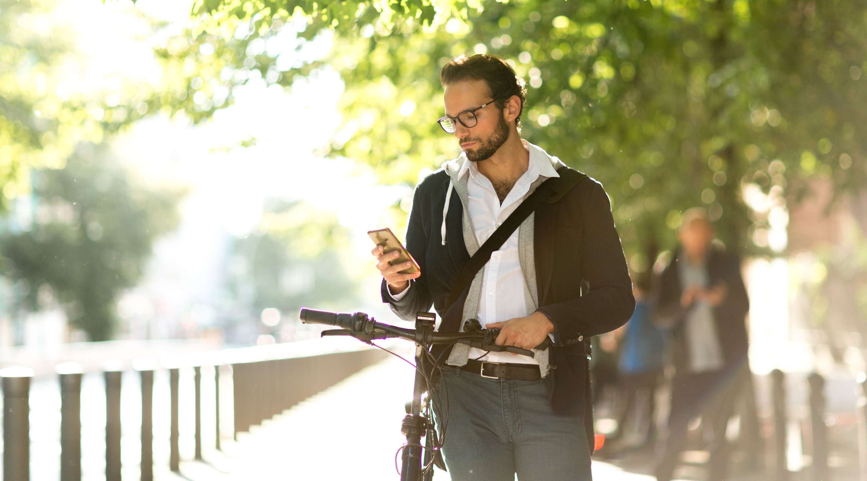 Mann schiebt ein Fahrrad und sieht auf ein Handy