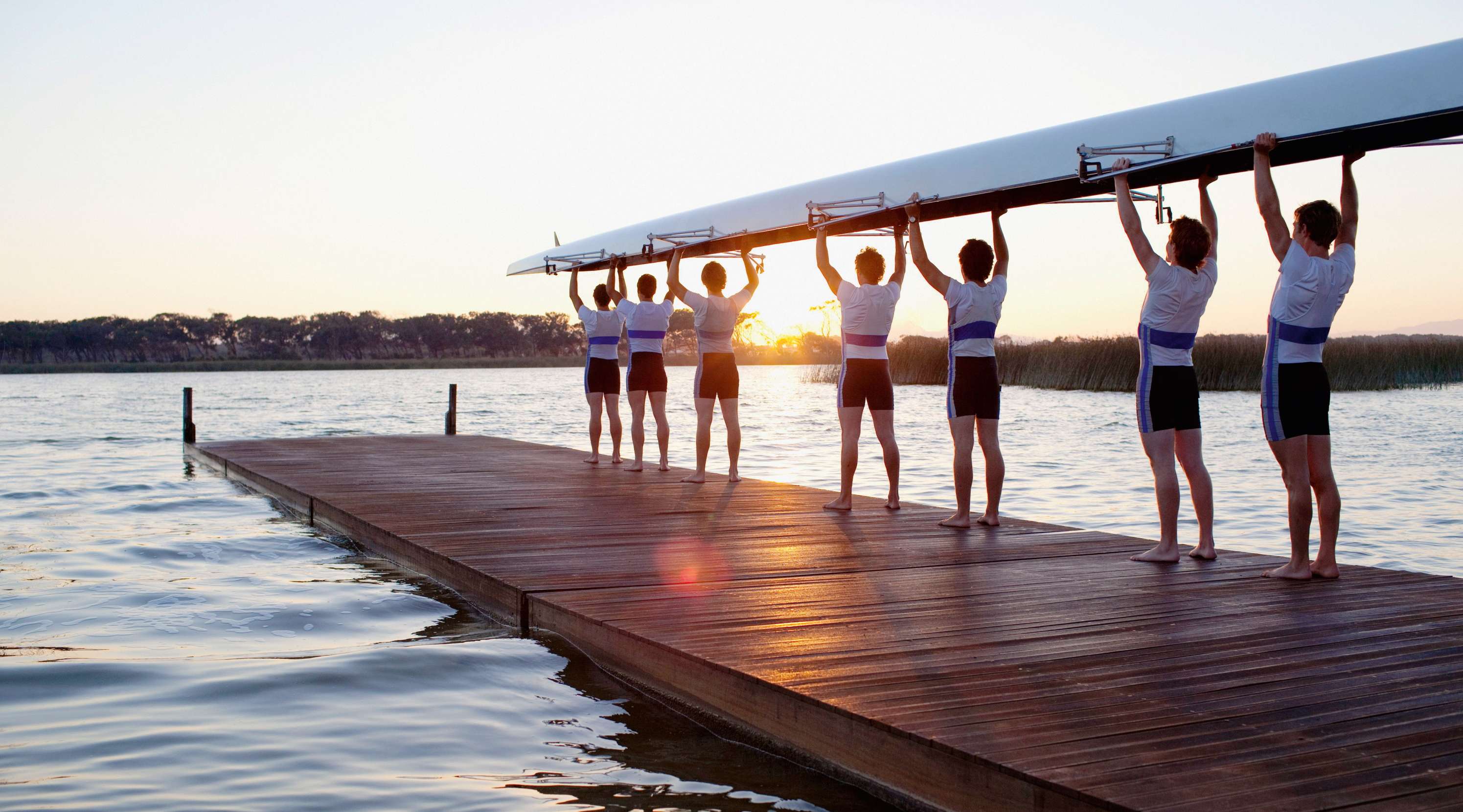 Männer stehen auf einem Steg und halten kopfüber ein Boot