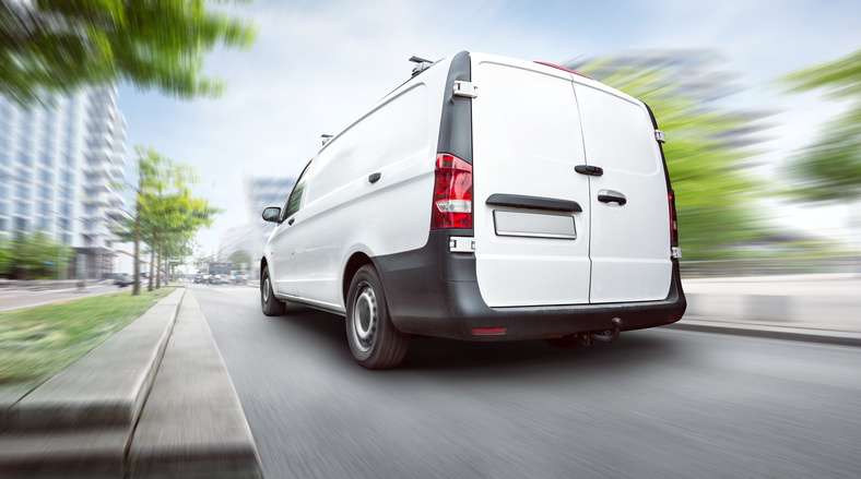 Ein Transporter fährt schnell durch eine begrünte Straße