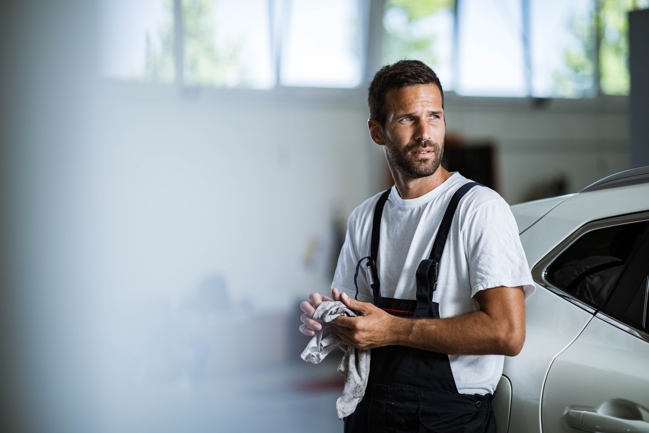 Arbeiter mit Latzhose lehnt an PKW