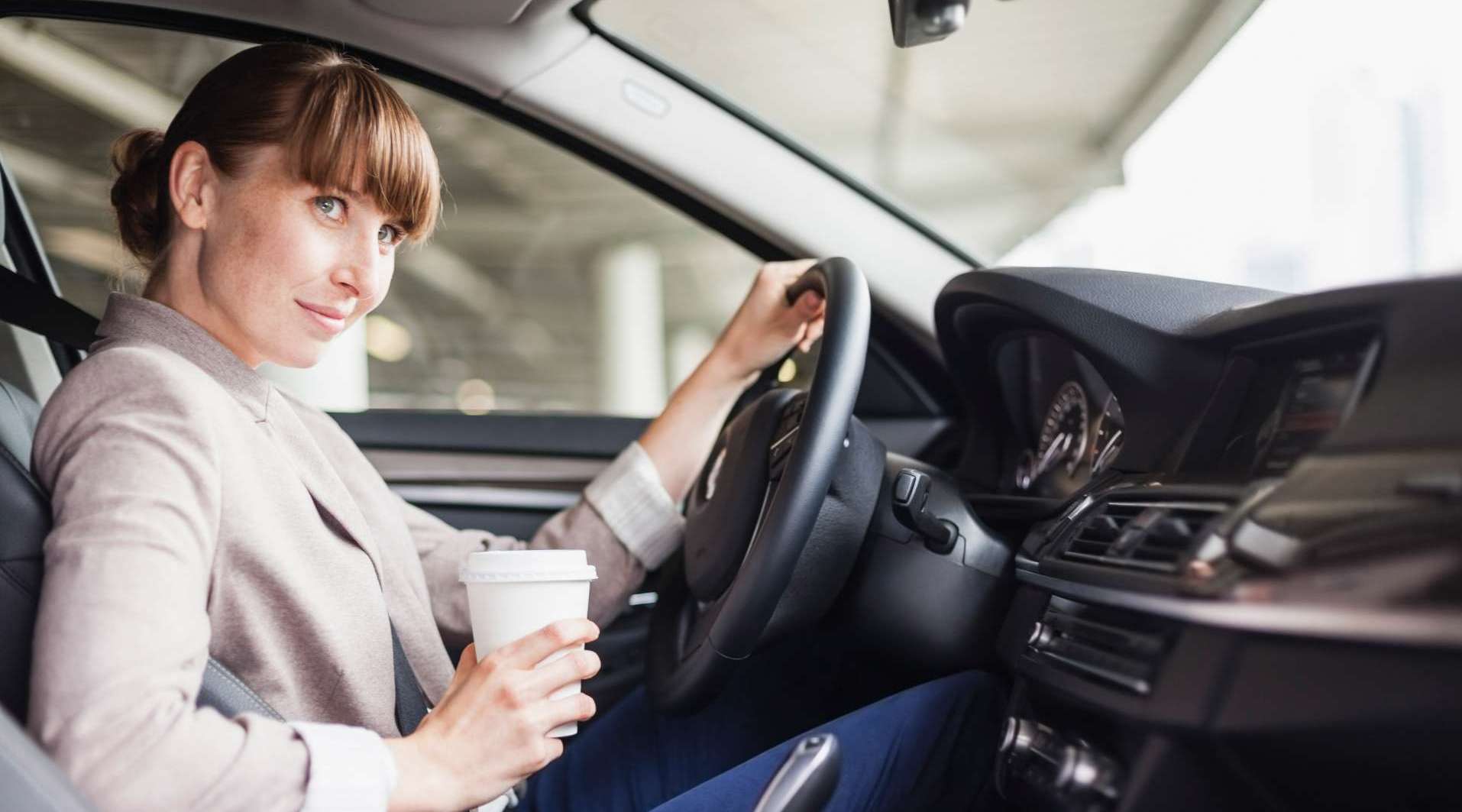 Frau mit Kaffee in der Hand steuert ein Fahrzeug
