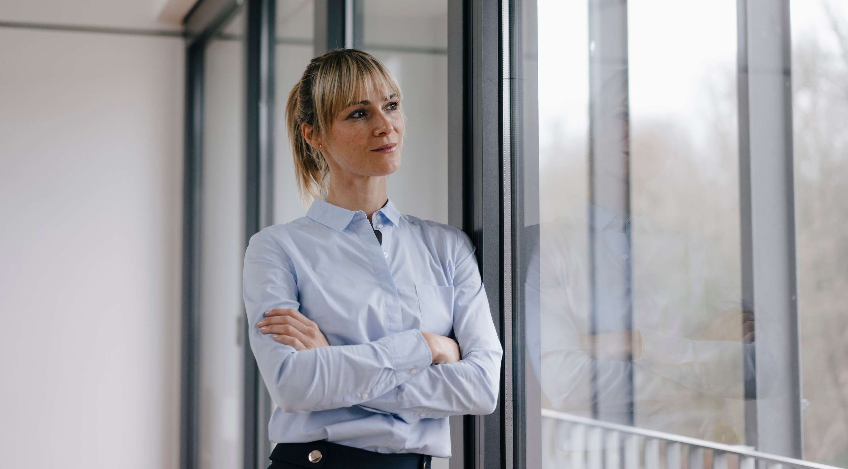 Frau mit verschränkten Armen steht vor einem Fenster