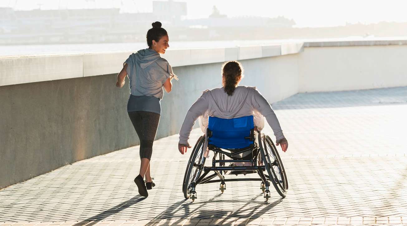 Laufende Joggerin unterhält sich mit Rollstuhlfahrerin 