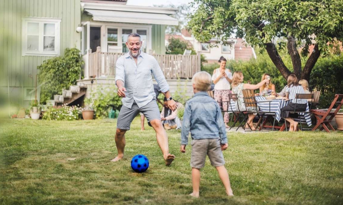 Mann und Kind spielen Fußball im Garten